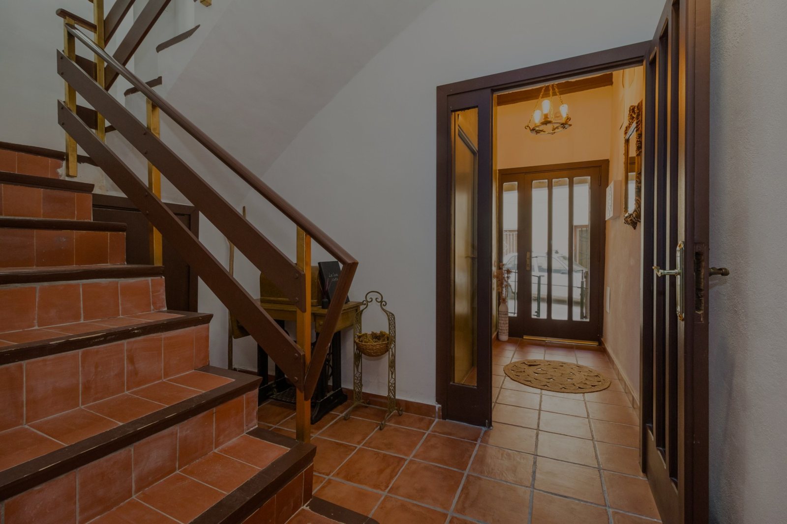 Escala de rajola i entrada de la casa, amb la llum càlida del rebedor